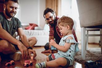 
		Homosexuelles Paar mit Tochter sitzen in einem Kinderzimmer und spielen miteinander
	